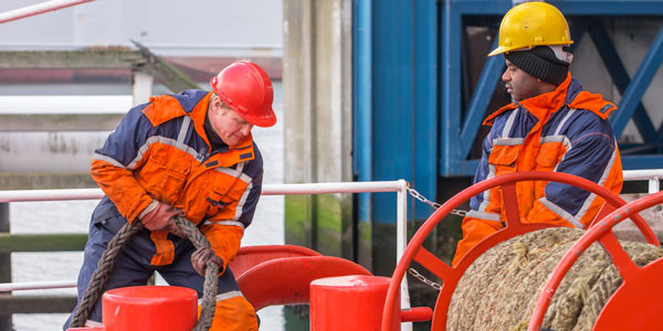 two engineers in orange high visibility pulling on ropes on a ship