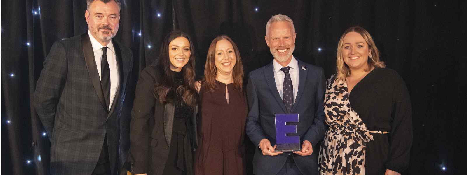 Head of Conferencing & Awards Gordon Hodge (second right, with trophy) with  Conferences Services Manager Katherine Boyling (third right) and Conferences Operations Manager Nicola Hyne (first right) at the E Awards. Also pictured: ceremony host Grant Stott and Becky Landells of award sponsor Saltire Hospitality. Photo by Paul Watt Photography