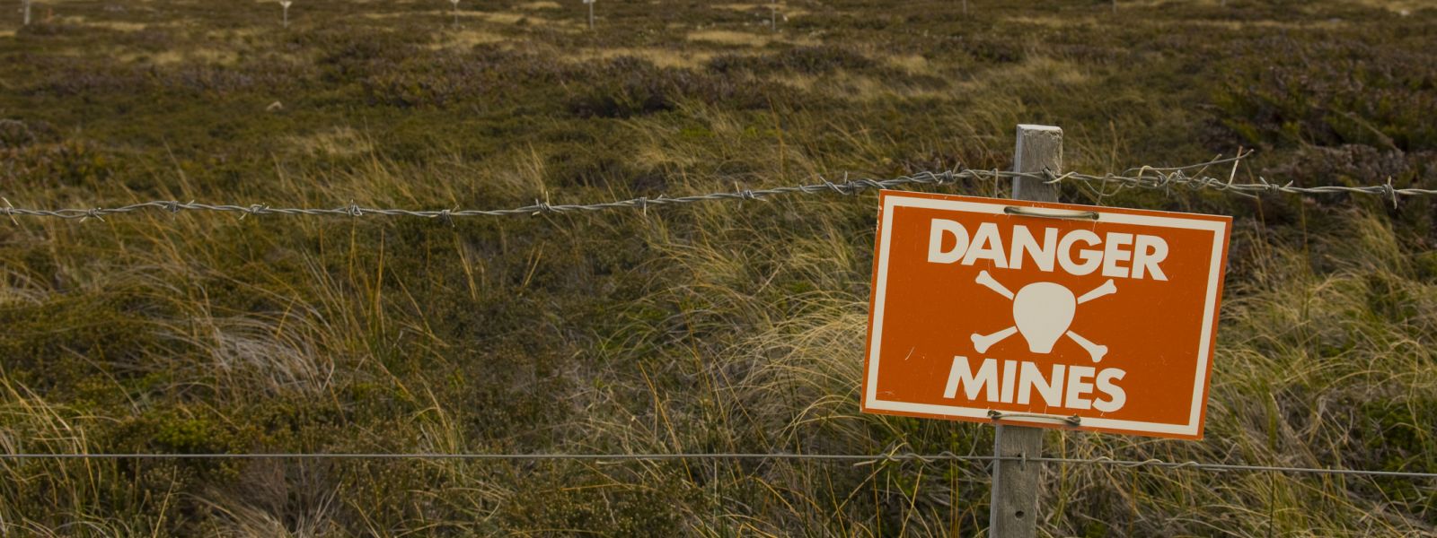 Landmine warning sign on fence in front of field.