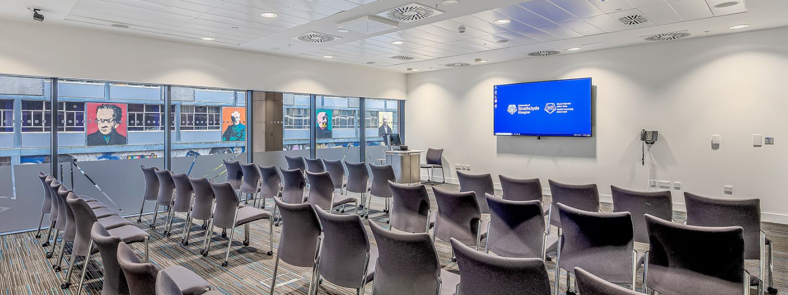 A Technology and Innovation Centre conference room set theatre style with rows of seats facing a large wall-mounted screen A Technology and Innovation Centre conference room set theatre style with rows of seats facing a large wall-mounted screen