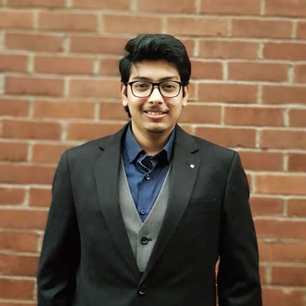 Business Analysis & Consulting student Chandrava standing against a brick background, smiling at the camera