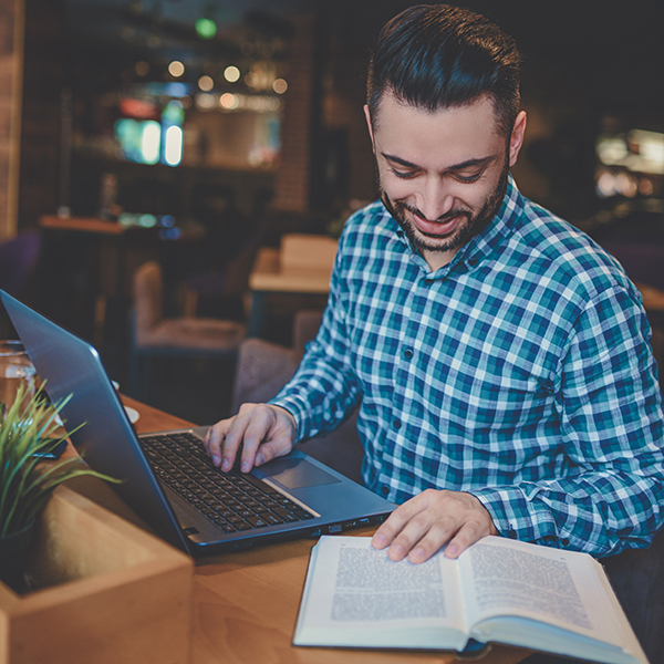 Male at desk with laptop and book