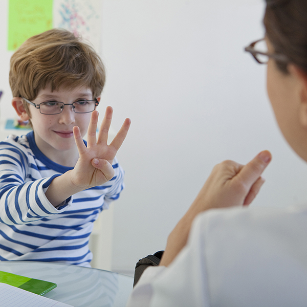 Child holds four fingers up while being assessed by a language therapist.