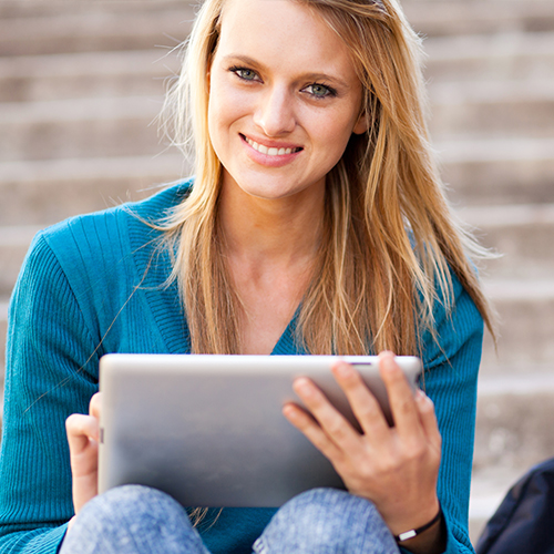 Female student sitting on steps looking at a tablet