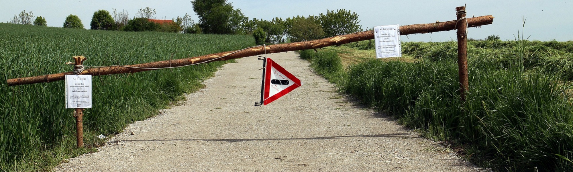 A country road blocked by wooden posts with a warning sign 