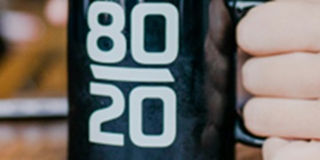 A hand holding a mug that says 80/20 on it