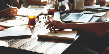 A hand writing in a book near a laptop