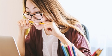 A girl facing a computer and biting a pencil A girl facing a computer and biting a pencil