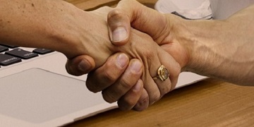 A laptop with a hand reaching out from the screen to shake another hand