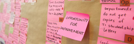 post it notes on a wall, the middle post it states opportunity for improvement