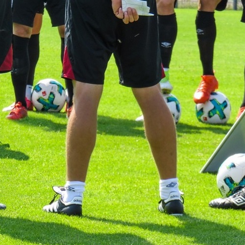 The legs of a group of footballers standing on a pitch with some footballs