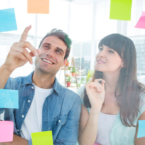 a man and a woman sit and point and ponder at postits