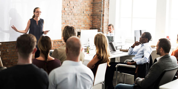 a woman gives a presentation to a room full of colleagues 