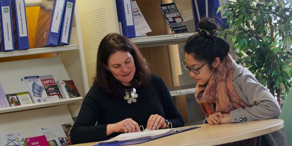 two women sit together at a table discussing documents in a folder