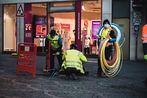 Three engineers wearing high vis vests working out in the street with large rolls of brightly coloured cables