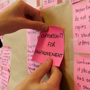 Hands putting a sticky note that says 'opportunity for improvement' onto a wall.