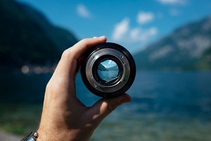 A hand holding a lens up with mountains in the distance