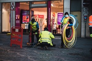 Three engineers wearing high vis vests working out in the street with large rolls of brightly coloured cables