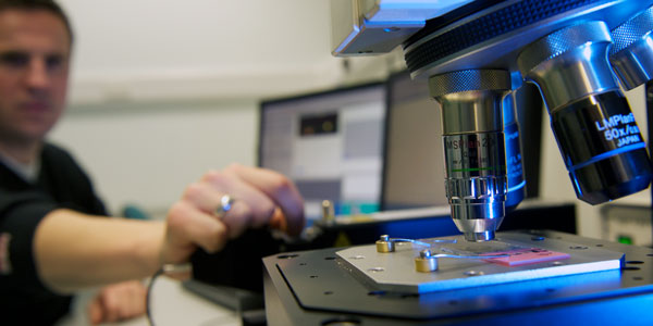 a researcher using a microscope and a computer to analyse a sample