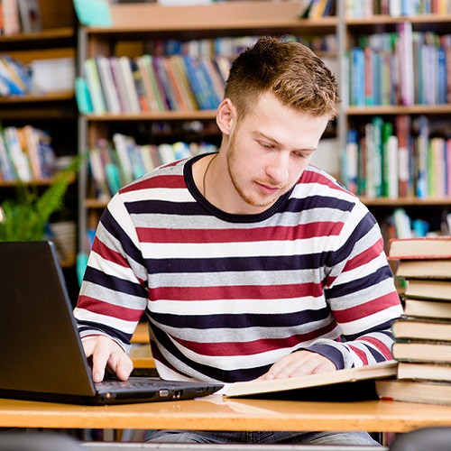 Male studying in library with laptop