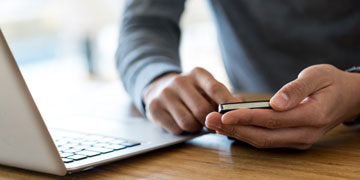 Close-up of a man in grey sweater sitting at wooden table next to laptop and holding mobile phone in both hands