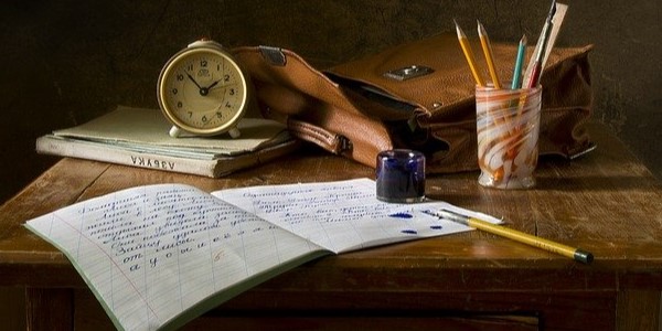 Picture of open notebook, pencil pot, ink and clock