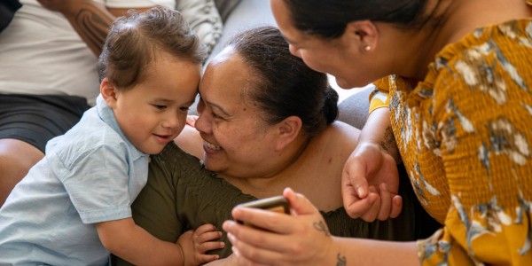 Two women and a toddler smiling and looking at a mobile phone