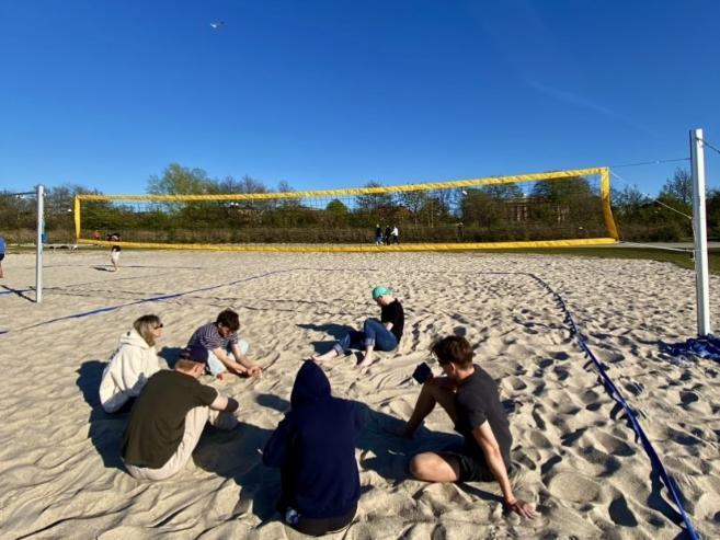 People sitting on a beach volleyball court on a sunny day