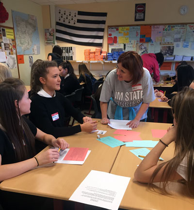 Kim Oliver talking and smiling with a grouo of school girls at a desk in a school