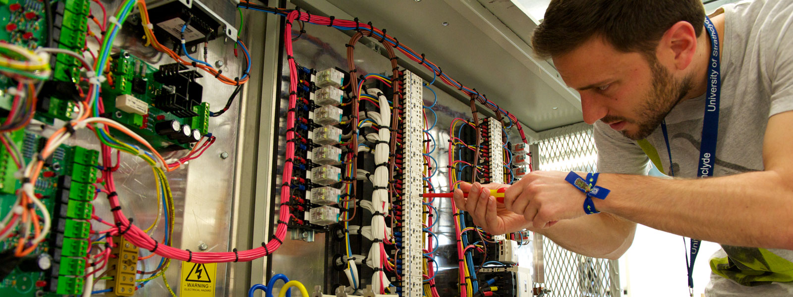 a researcher using a screwdriver on a large piece of equipment covered in colourful wires