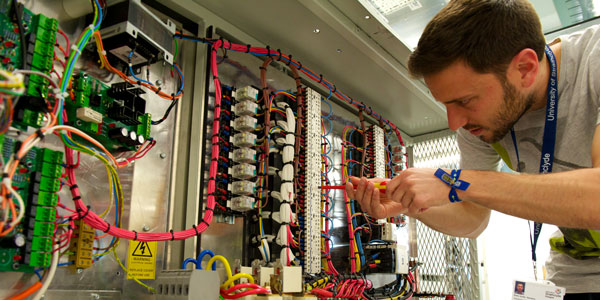 a researcher using a screwdriver on a large piece of equipment covered in colourful wires