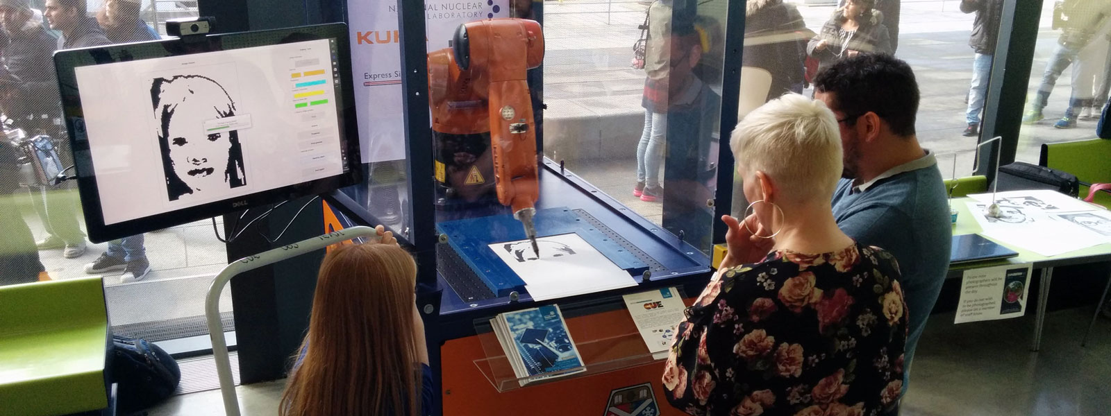 people standing looking at an orange robotic arm