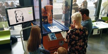 people standing looking at an orange robotic arm