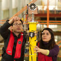 two students working on the top of a yellow pole with a screwdriver