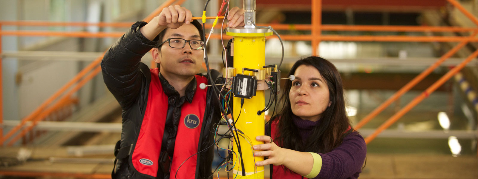 two students working on the top of a yellow pole