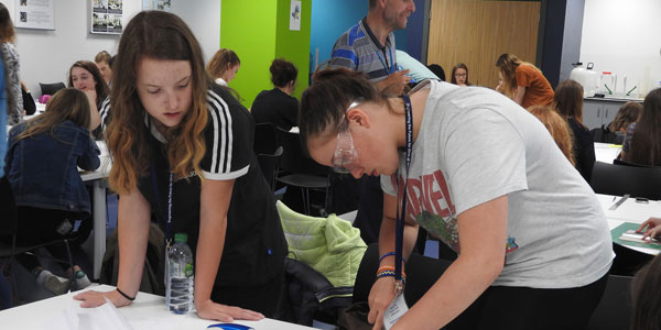 two female students bending over a desk working during the Young Weir Wise programme