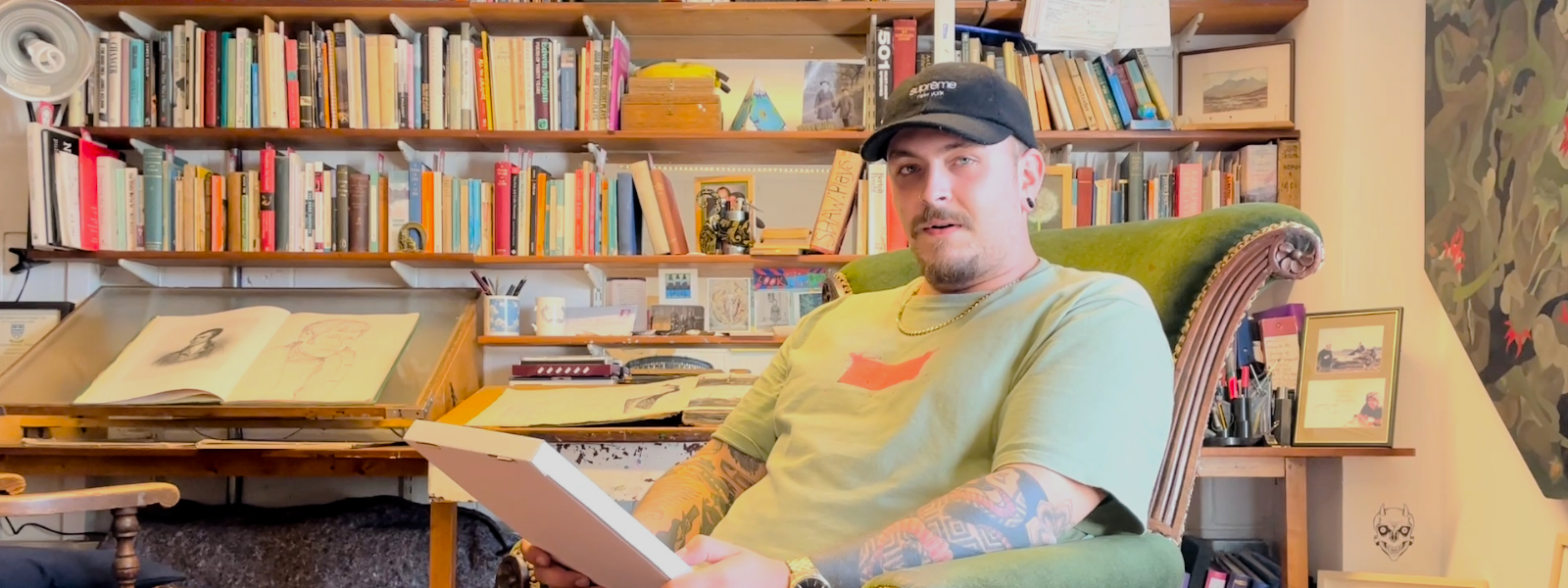 A man sits in a green armchair in front of a colourful bookcase