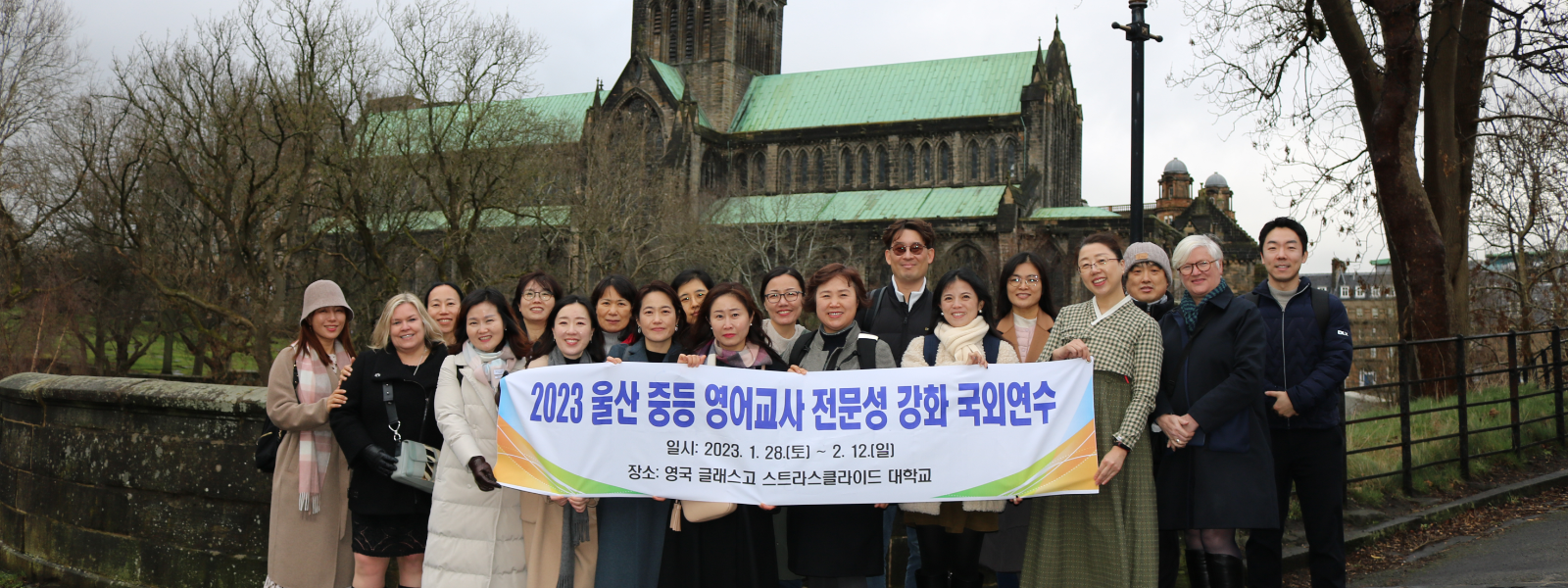 A group of people stand in front of Glasgow Cathedral holding a banner with Korean writing
