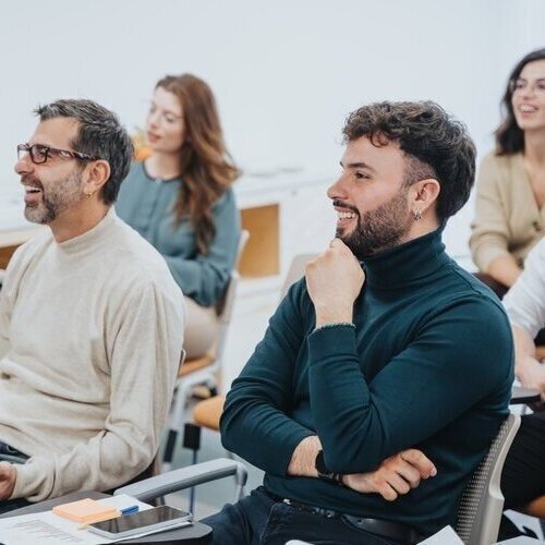 A multi generational, group of adult students with positive expressions engaged in a learning activity during a workshop, displaying attentiveness and interaction in a modern classroom setting.