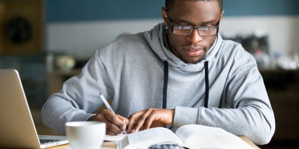 Focused millennial student in glasses making notes writing down information from book in cafe preparing for exam