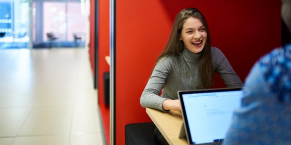 A laughing girl sitting in a red booth in front of a laptop