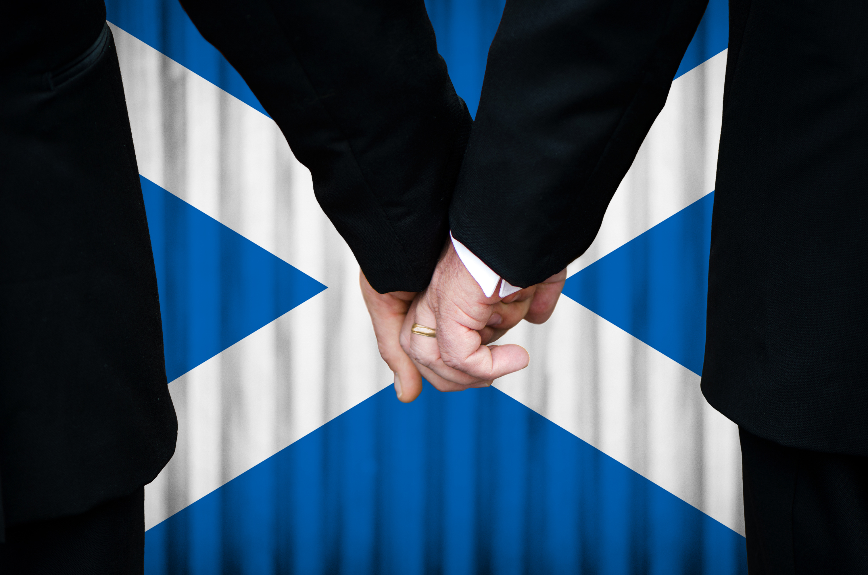 Same sex couple holding hands in front of Scottish saltire
