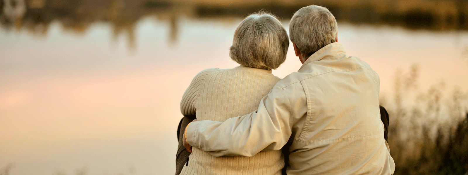 elderly couple sits together looking out at a lake