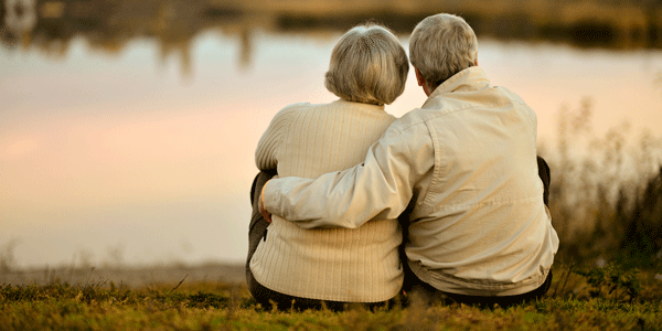 elderly couple sit side by side at a lake