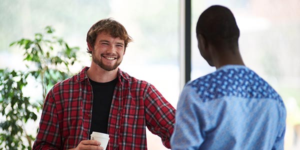 Two students talking, one holding a cup.