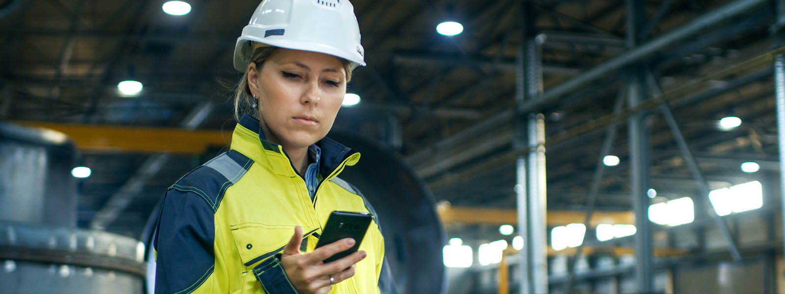 Woman in hi-vis jacket and hard hat looking at her phone.