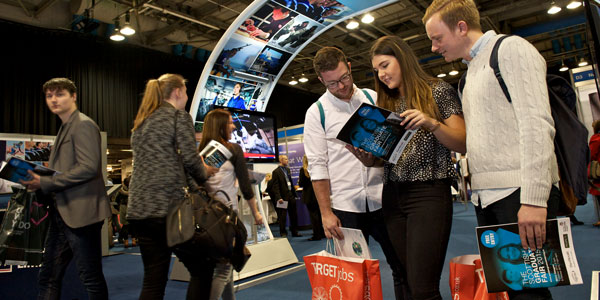 three graduates at a graduate fair looking at brochures together