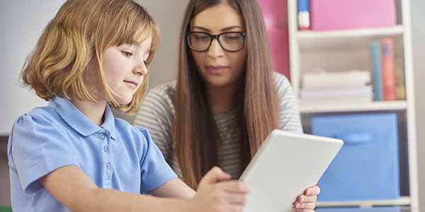 a classroom assistant listens as her student explains what she is reading on a digital tablet .