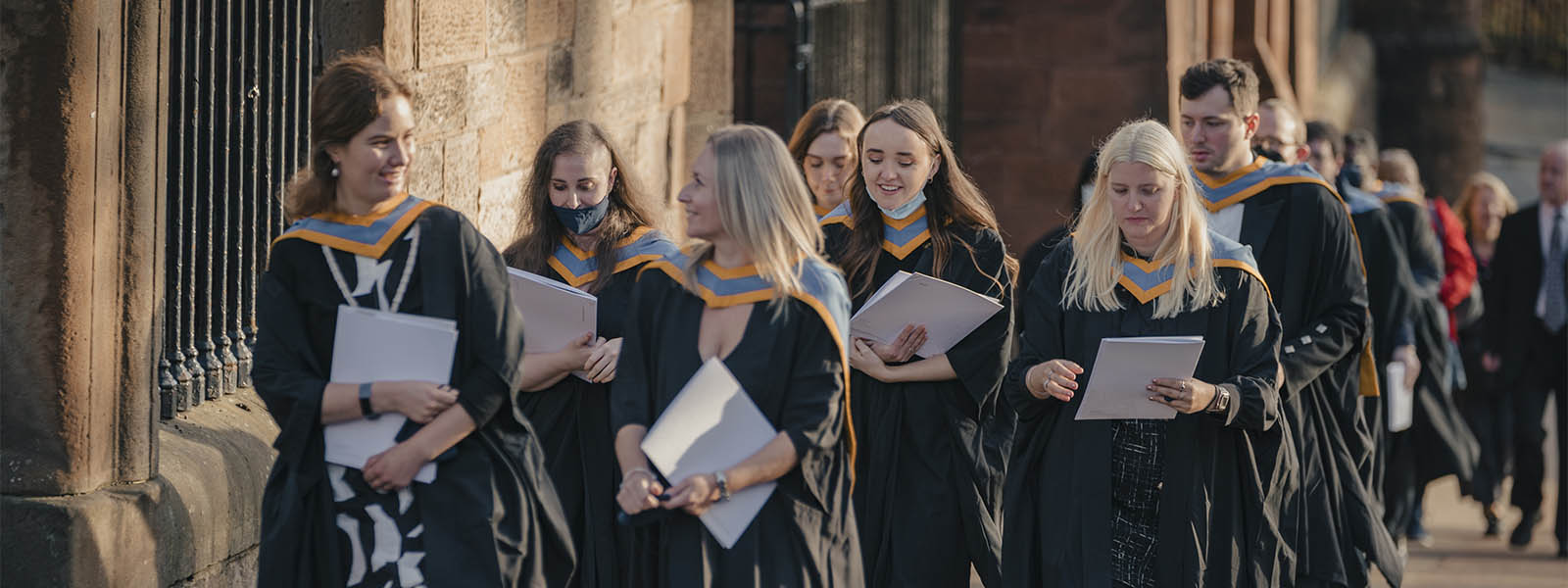 Graduates walking outside the Barony Hall wearing their graduation gowns.