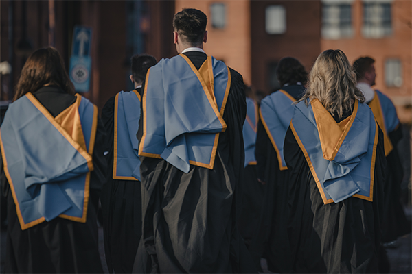 Group of students wearing graduation gowns, walking away from the Barony.